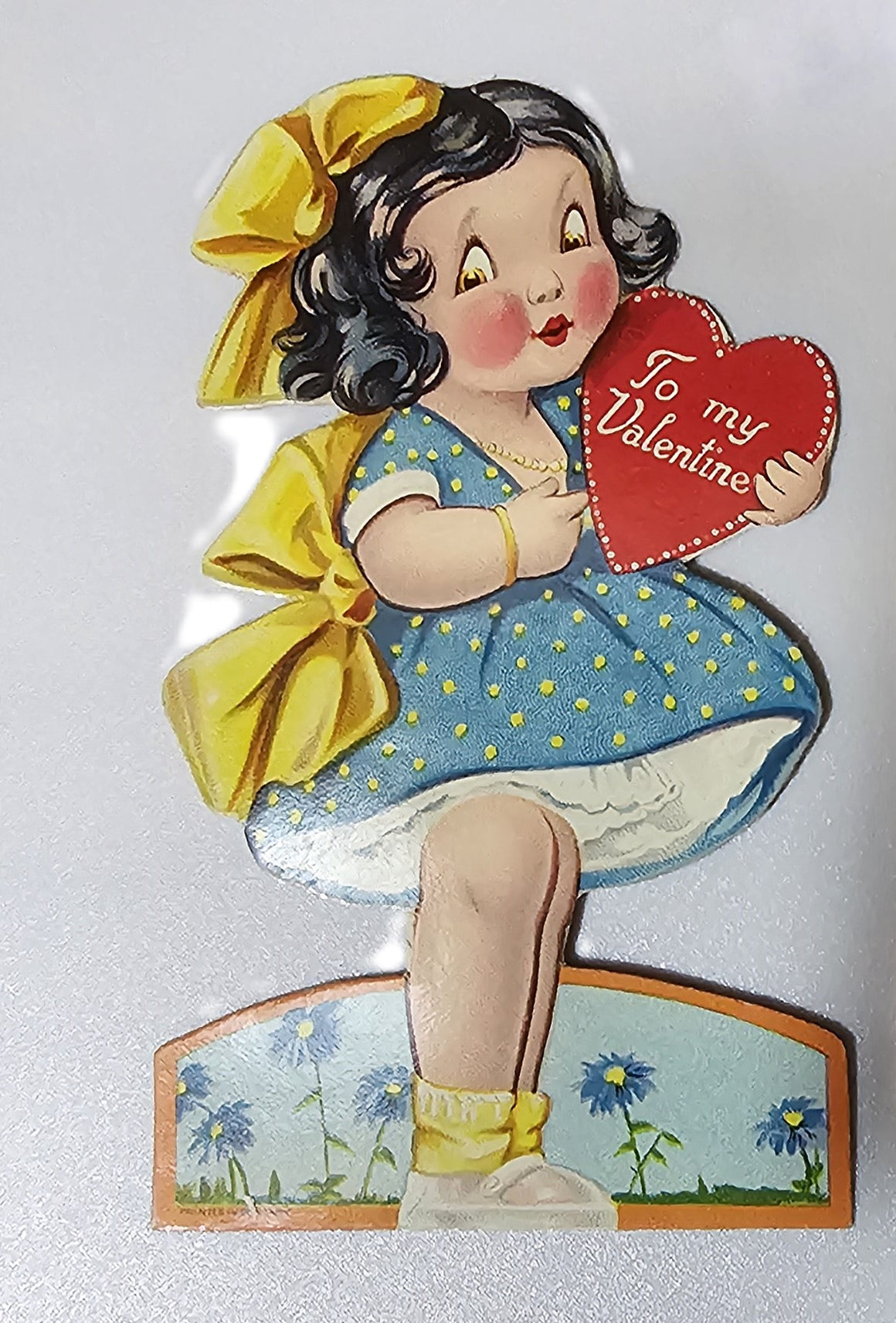 Vintage Die Cut Valentine Card Little Girl in Blue Polka Dot Dress with Yellow Ribbons Holding Red Heart
