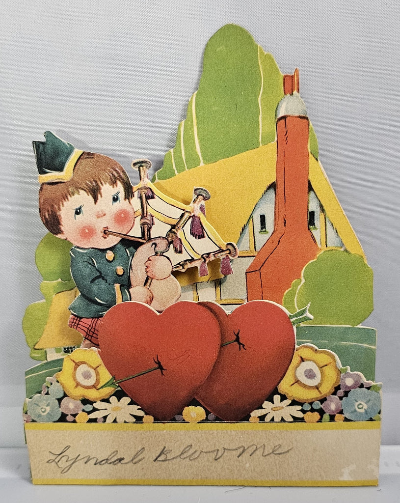 Vintage Die Cut Valentine Little Scottish Boy Playing Bagpipes Outside a Cottage with Hearts and Puppy Dog