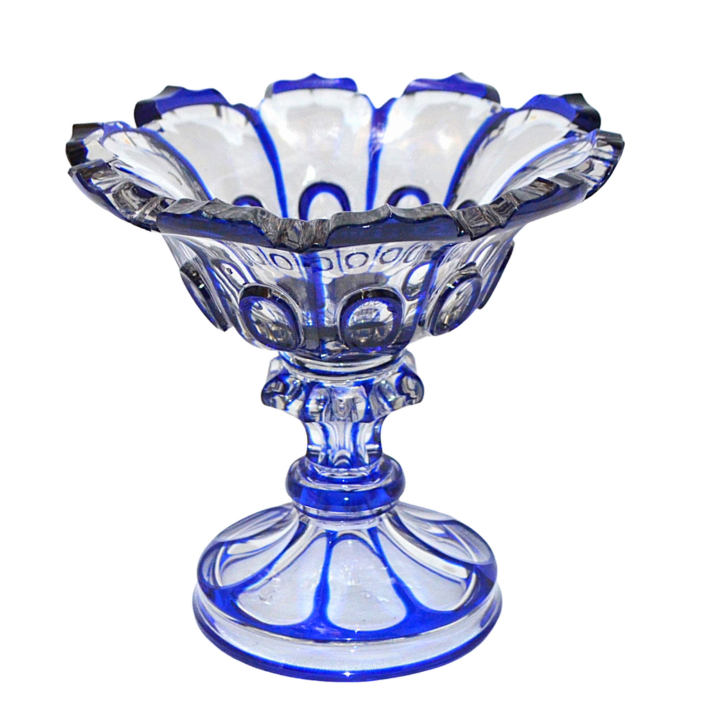 A vintage cobalt blue and clear glass pedestal bowl with a scalloped rim and decorative cut-glass details, shown on a plain white background.