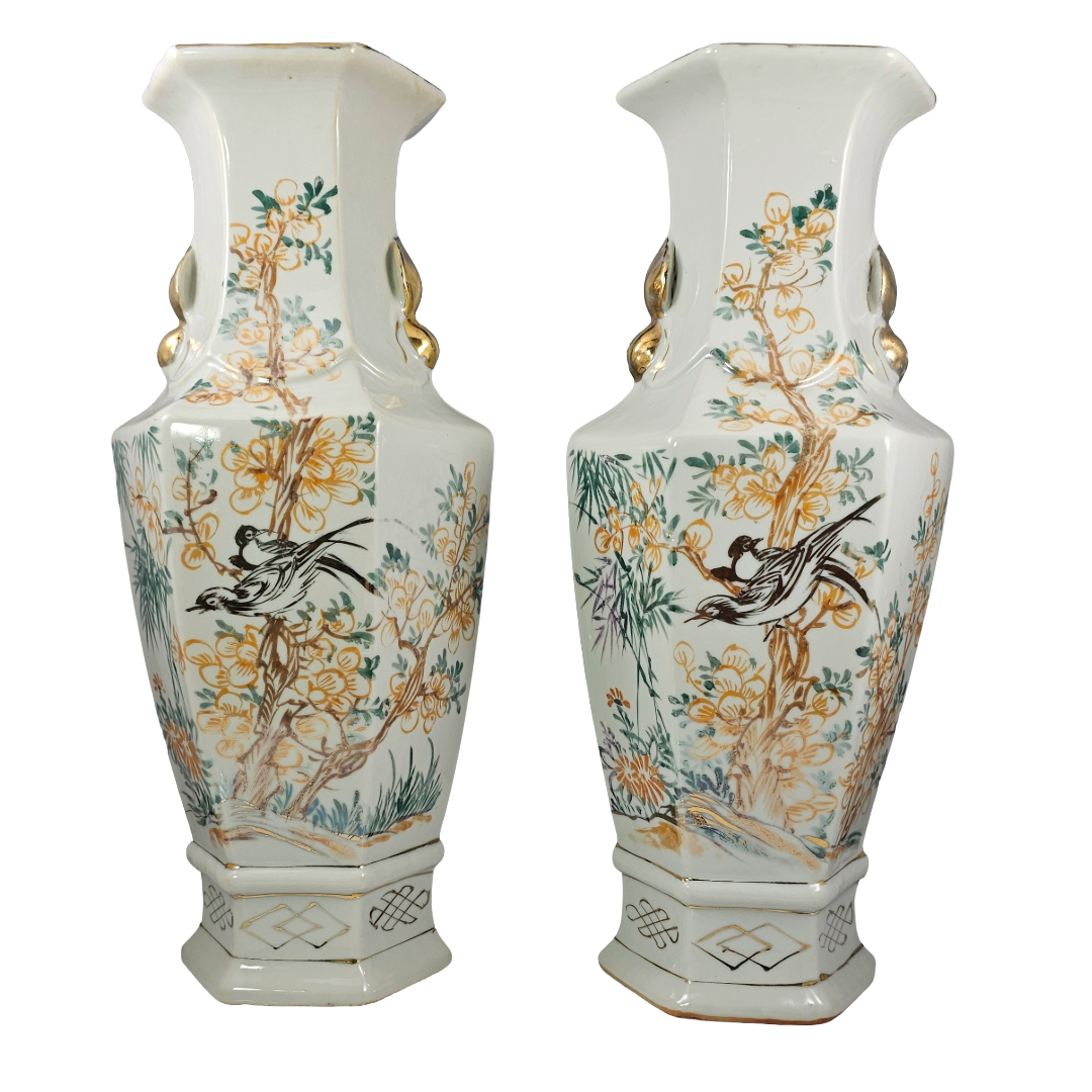 A pair of tall, hexagonal ceramic vases with a white glaze, decorated with hand-painted floral motifs, birds, and gold accents.