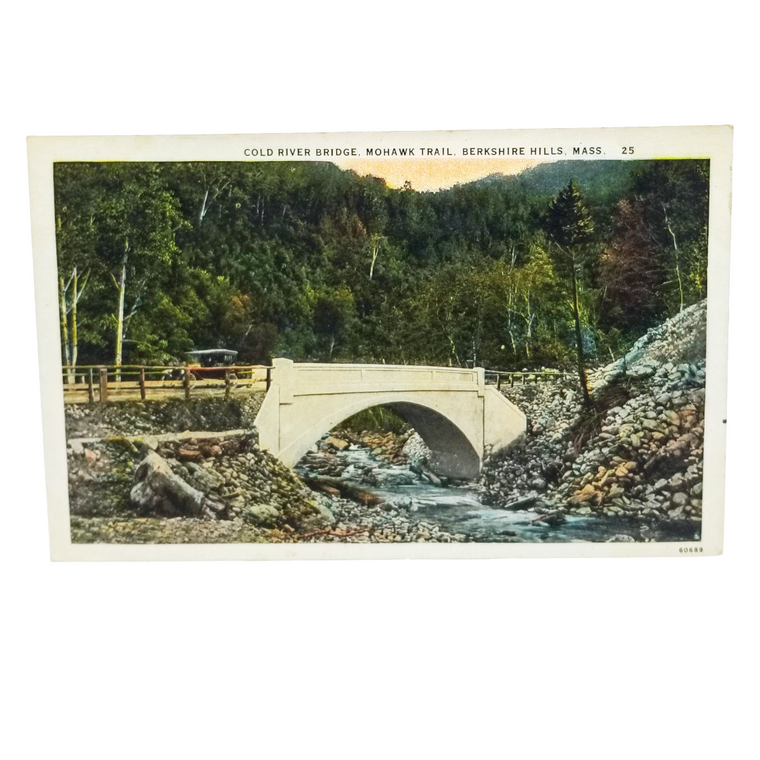 A vintage postcard showing Cold River Bridge in Mohawk Trail, Berkshire Hills, Massachusetts. The postcard features a printed landscape with a stone bridge over a rocky stream, surrounded by dense green and brown forest, with a small vintage car on the left side.
