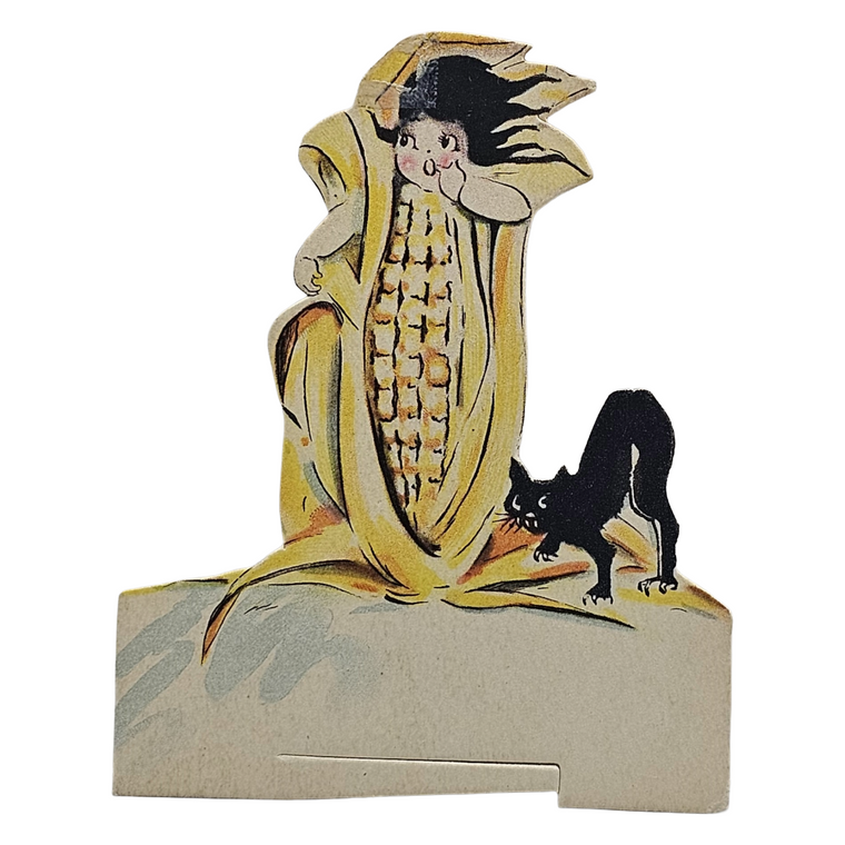 Decorative paper cutout of a corn stalk with a face and a black cat on a white background