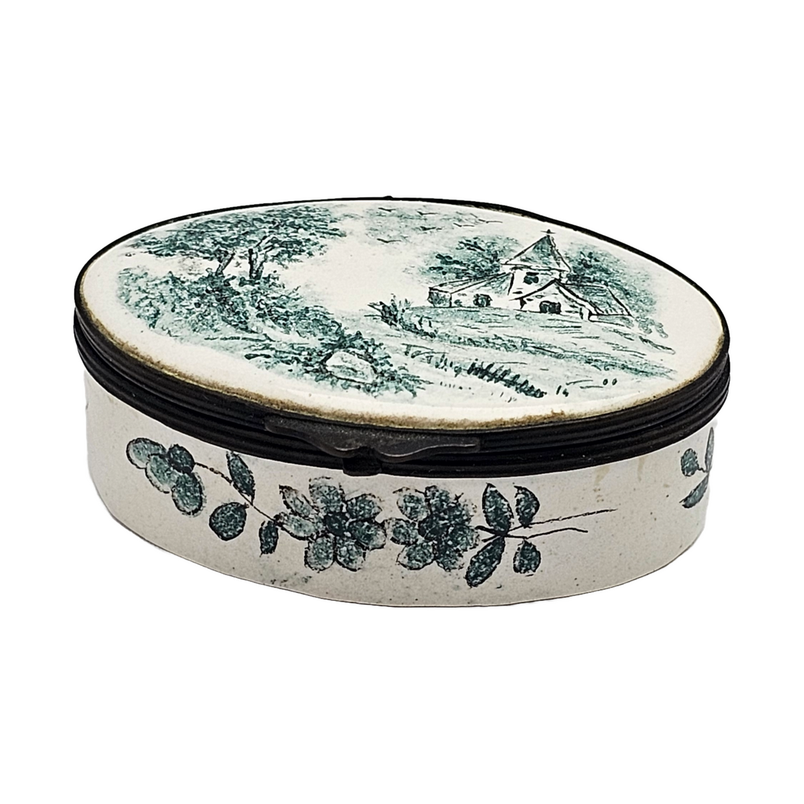 An oval-shaped, hand-painted French Faience trinket jar with a green enamel church scene on the lid and floral patterns around the base.