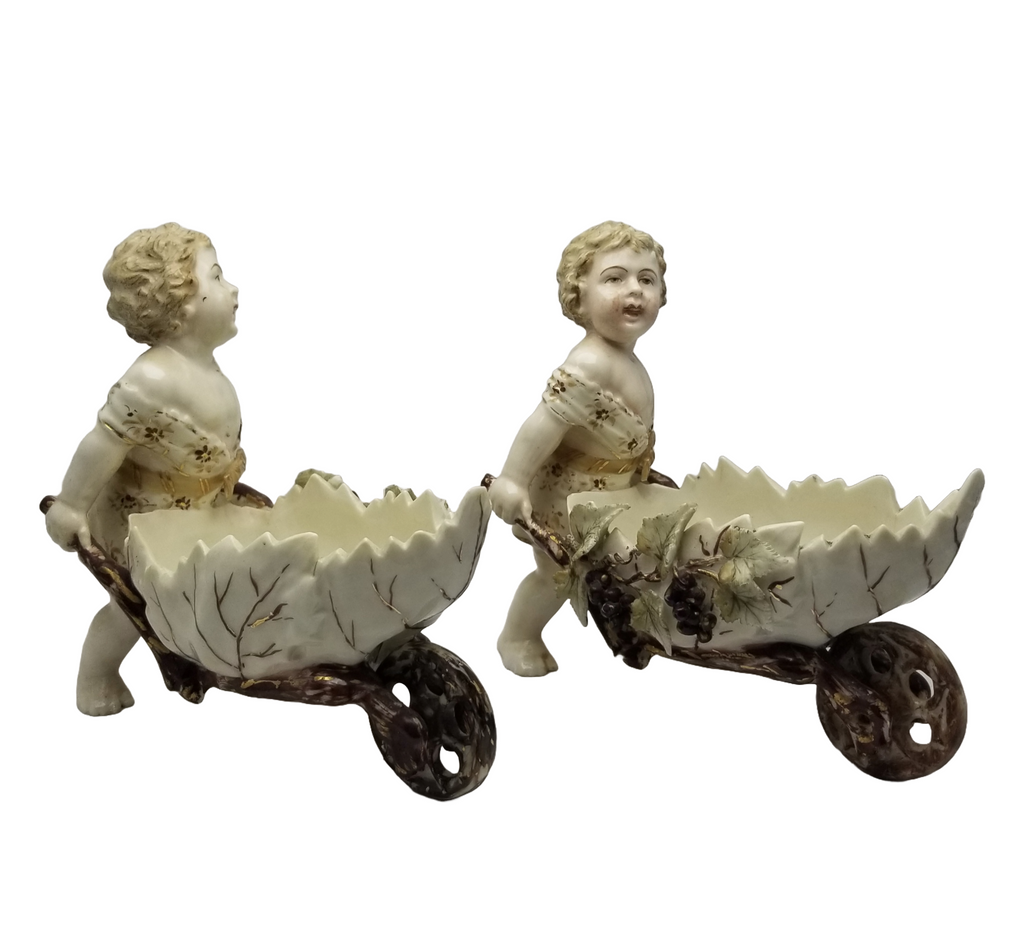 German Porcelain Bisque Garden Cherubs Pair Putti Hand Painted Pushing Wheelbarrows with Moving Wheels Volkstedt Thuringia