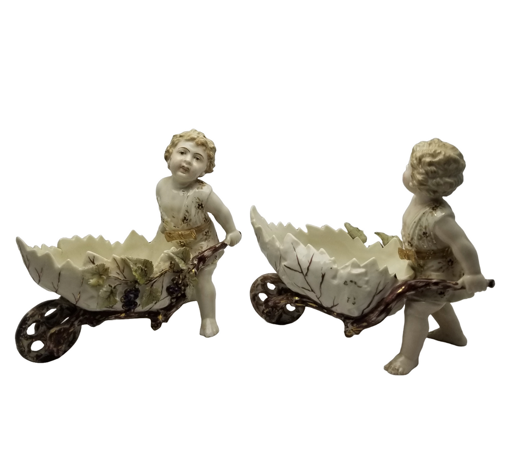 German Porcelain Bisque Garden Cherubs Pair Putti Hand Painted Pushing Wheelbarrows with Moving Wheels Volkstedt Thuringia