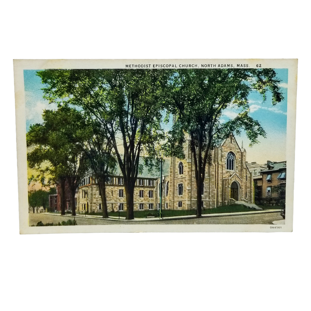 A vintage printed postcard showing the Methodist Episcopal Church in North Adams, Massachusetts, with tall green trees in the foreground and a light blue sky. The postcard has a white border with printed text at the top and a small printed mark at the bottom right.