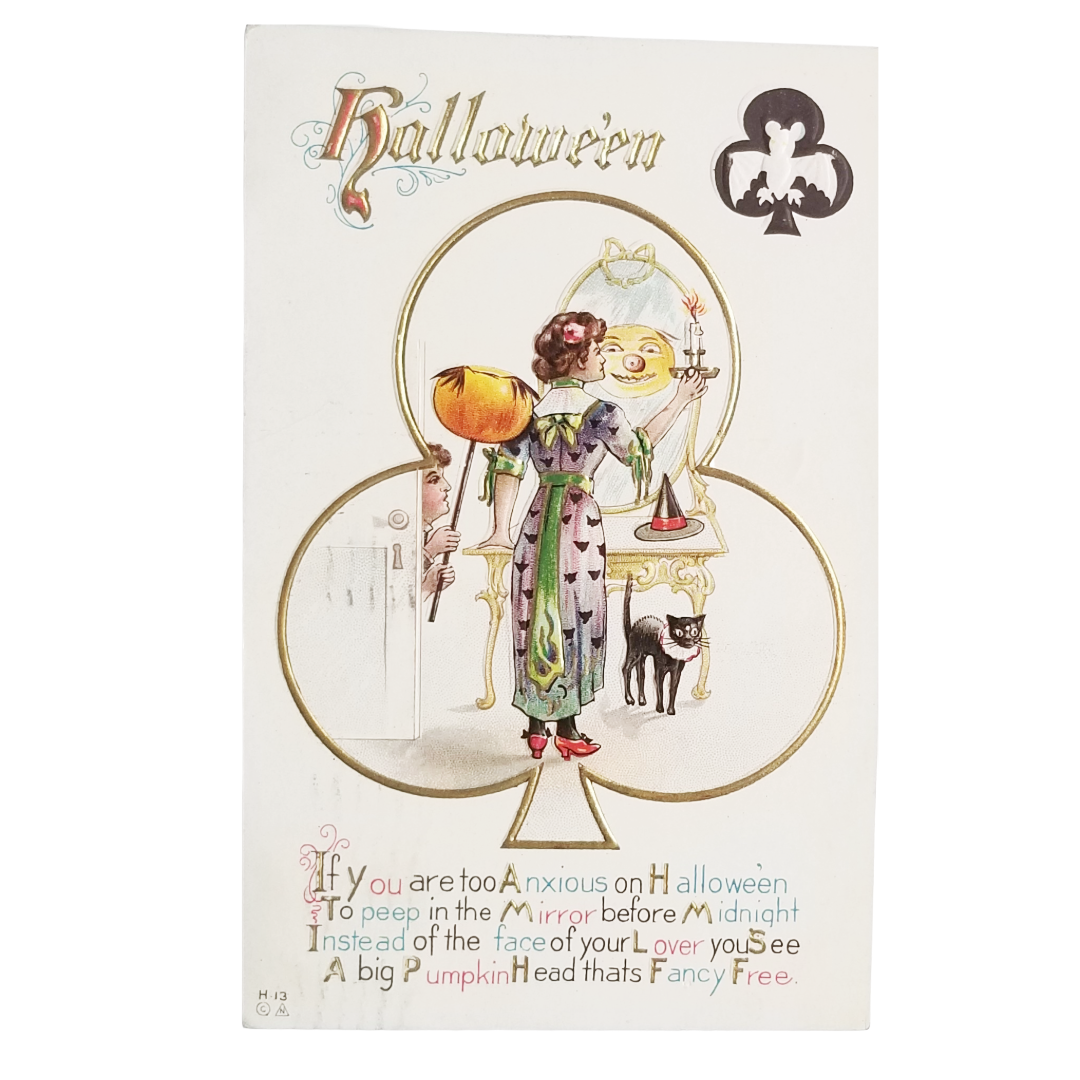 Vintage Halloween greeting card featuring an illustration of a woman in a green dress looking into a mirror with a pumpkin and a black cat, with decorative text and a club suit symbol.