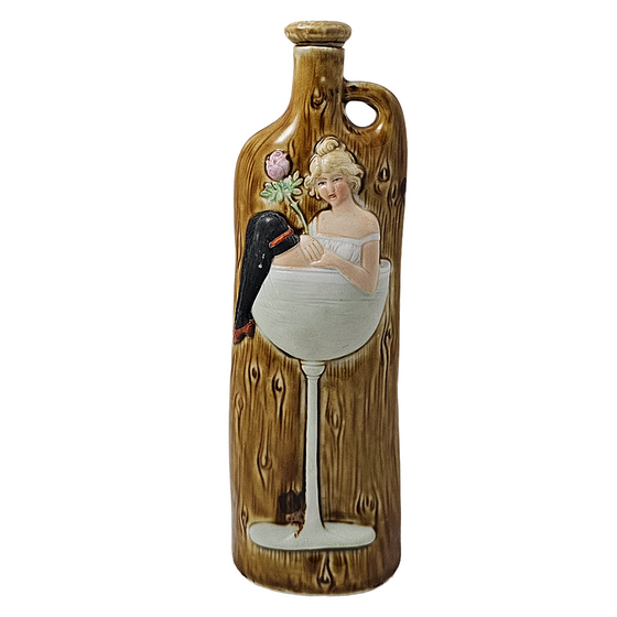 Decorative bottle with artistic design of a woman and a dog in a wine glass on a wooden background.